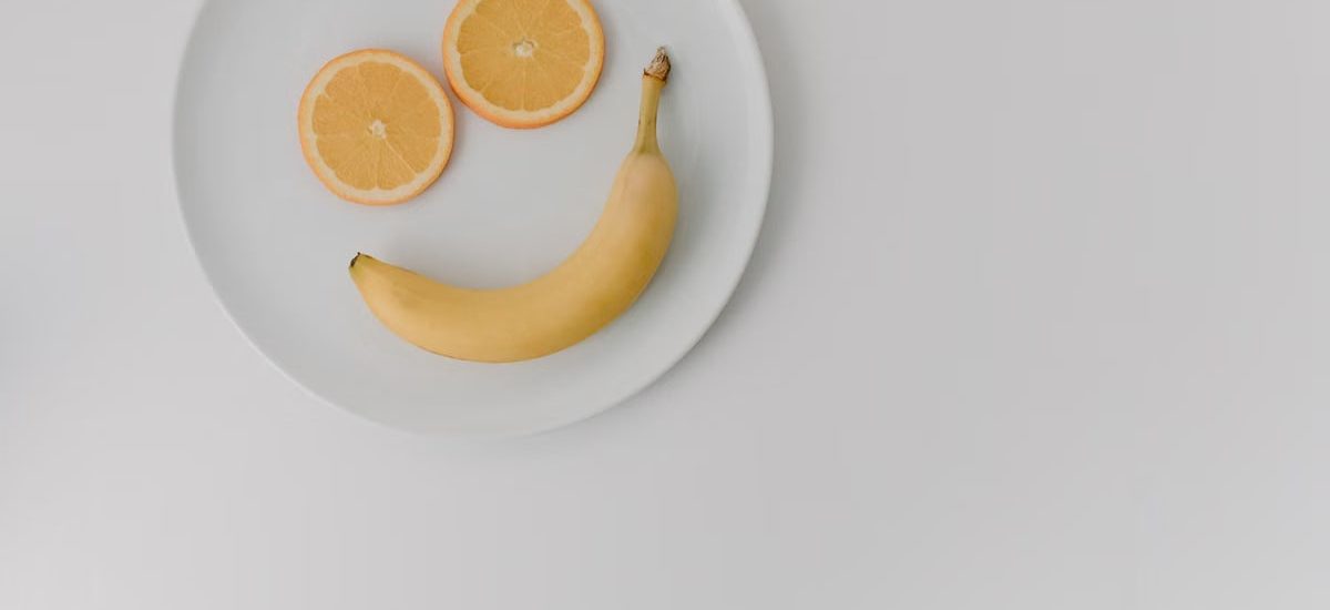 A playful arrangement of banana and orange slices forming a smile on a white plate.