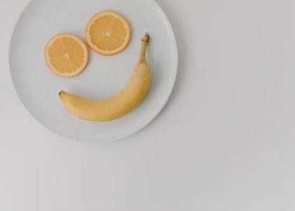 A playful arrangement of banana and orange slices forming a smile on a white plate.